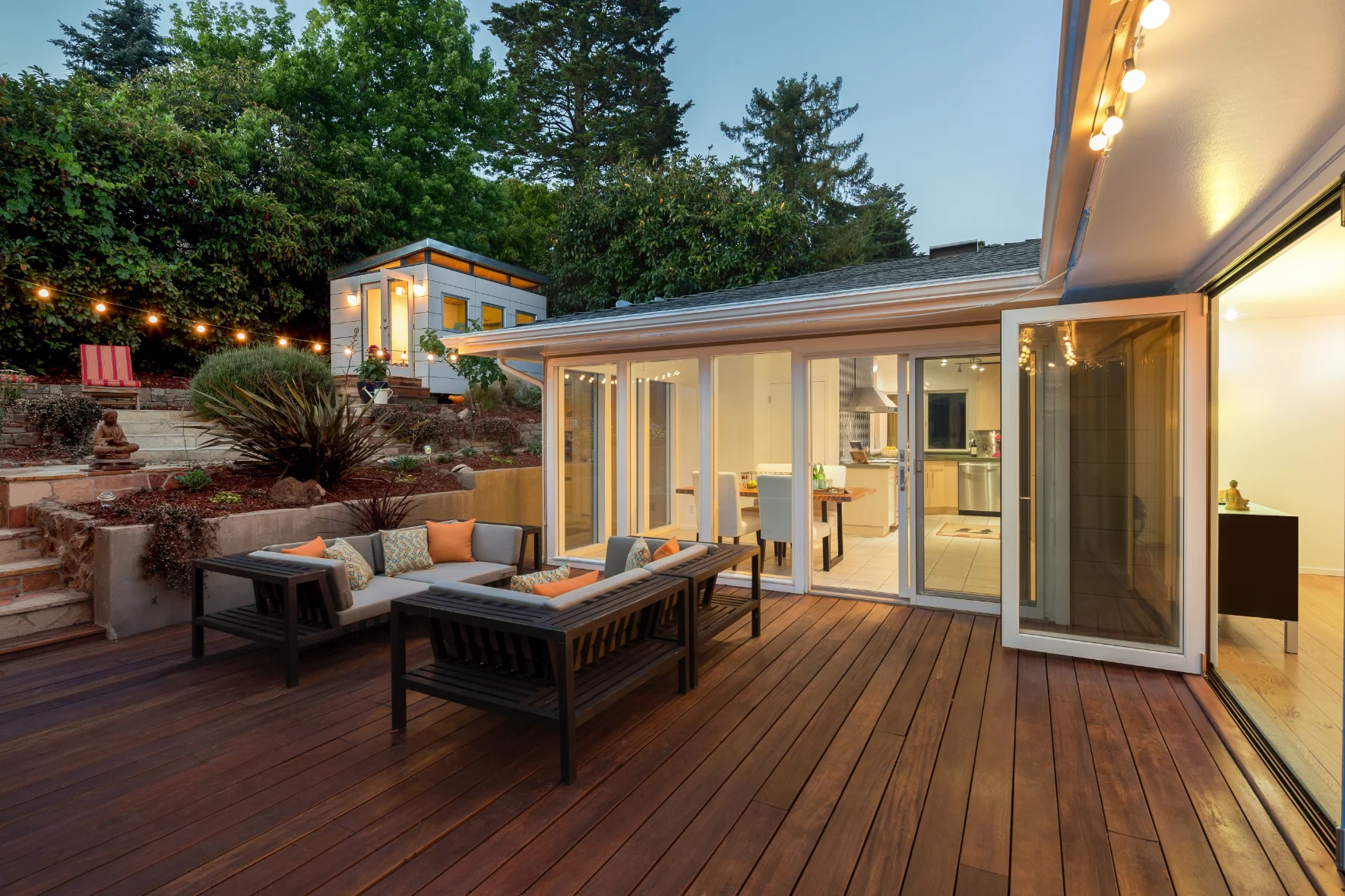 Evening view of a cozy patio with furniture adjacent to a lit-up modern home