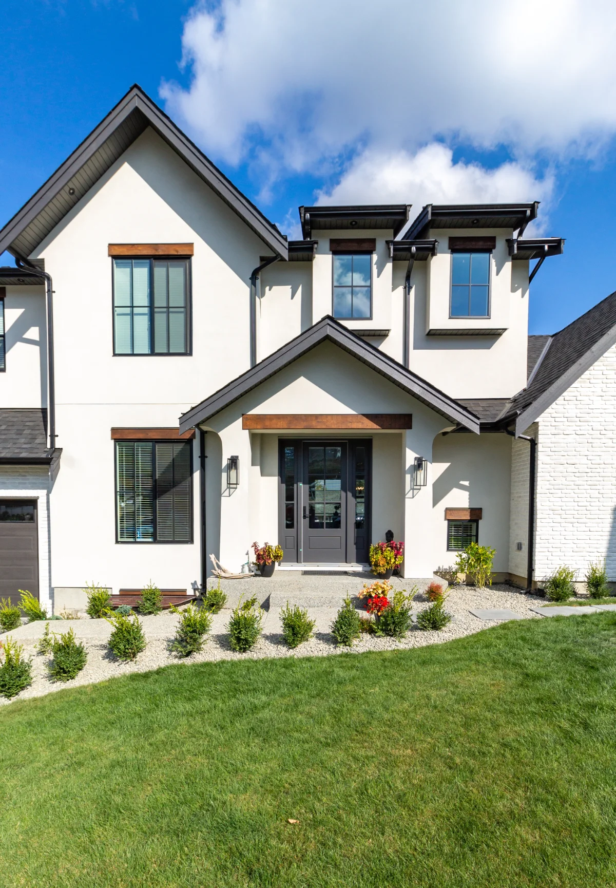 Modern two-story house with a white and black exterior, landscaped garden, and clear blue sky