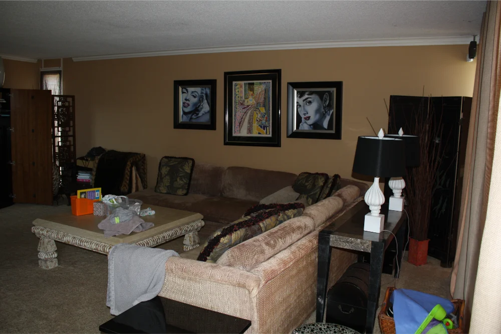 A living room with a sectional sofa, stone coffee table, and framed artwork—part of a whole home remodel—features table lamps and various items scattered throughout the inviting space.