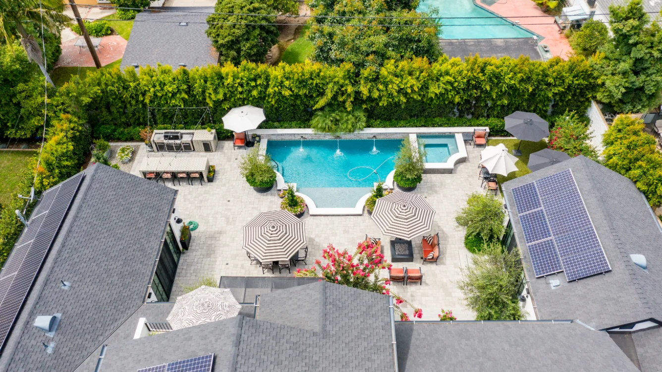 Aerial view of a backyard with a swimming pool, hot tub, lounge chairs, umbrellas, and solar panels on rooftops—showcasing a stunning Custom Home Build in Santa Ana, CA.