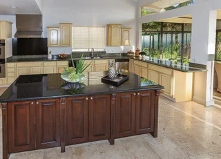 Modern kitchen with light wood cabinets, a dark wood island with black countertops, large windows, and tile flooring.