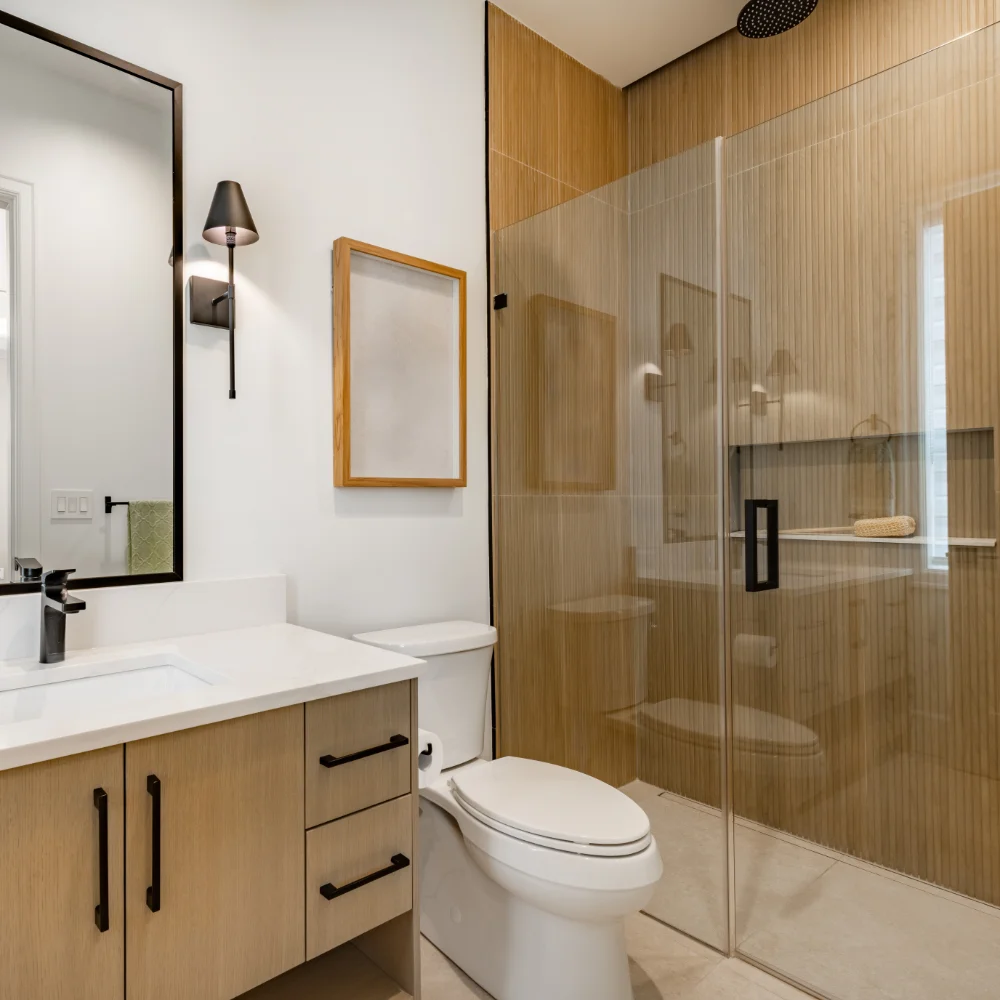 Modern bathroom with light wood cabinetry, white countertop, wall-mounted mirror, black fixtures, toilet, and a glass-enclosed shower—ideal for house extensions or room additions seeking a fresh, contemporary look.